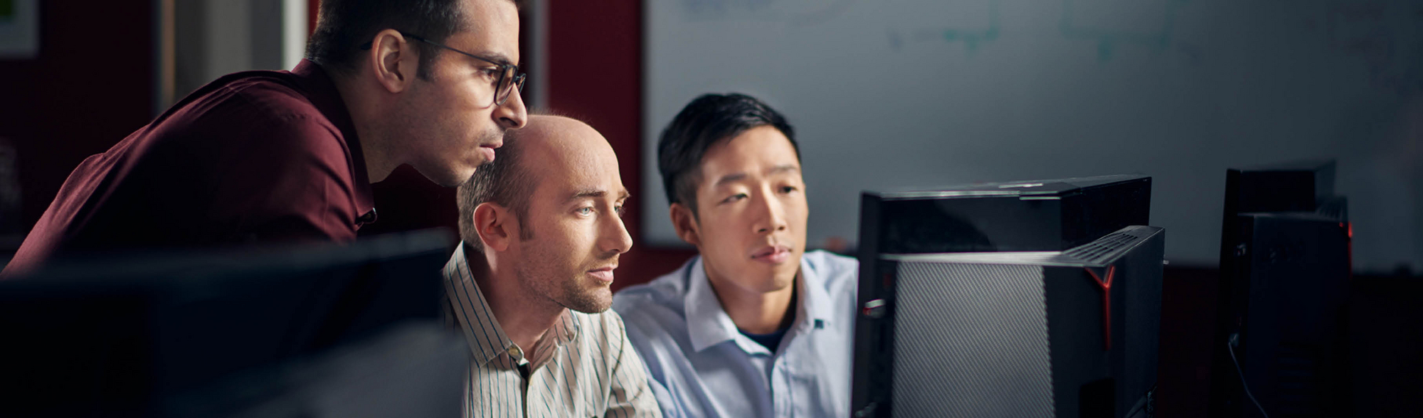 Three of our employees sit in front of a screen and work together on the further development of our VirtualLab Fusion software.