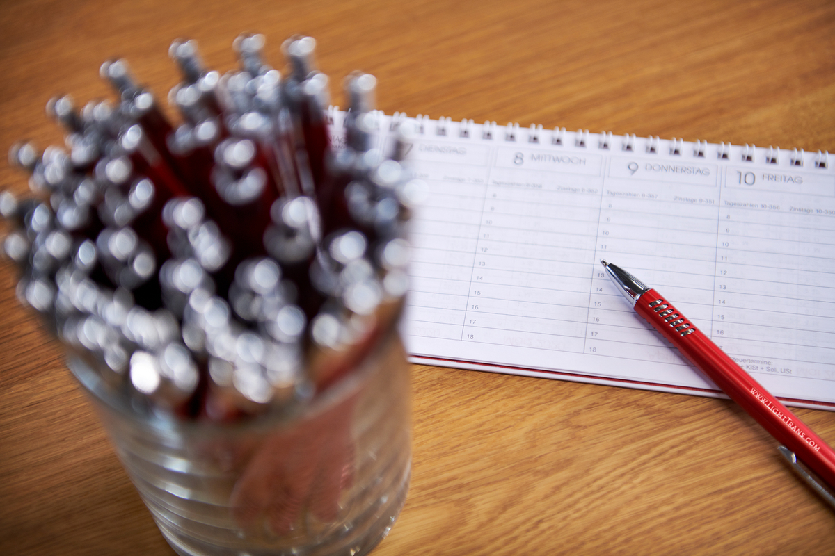 A glass full of LightTrans pens is on a table and behind it is a calendar.